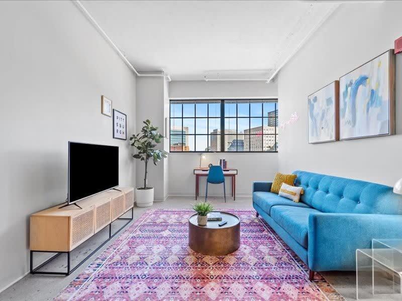 uma sala de estar com um sofá azul e uma televisão em CozySuites Trendy 1BR, Downtown Pittsburgh em Pittsburgh