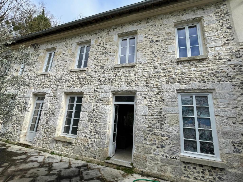 Cette ancienne maison en pierre est dotée d'une porte et de fenêtres. dans l'établissement Le Grand Logis du Château de Ste Geneviève-3 Chambres-Salon-Cuisine-Terrasse-Barbecue-100 M2 pour 6 à 8-Havre de Paix-3Ha à 3Km de Giverny-Parc Naturel du Vexin-Piscine En Été-En Sus Massages-Jacuzzi-Sauna-Hammam-Fitness-Ballades en 2CV-Vélo-Cheval-Avion, à Sainte-Geneviève-lès-Gasny