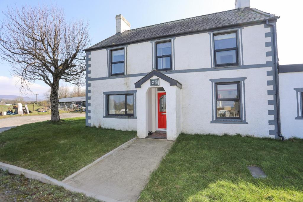 a white house with a red door on a street at Bryn Afon Farm in Caernarfon