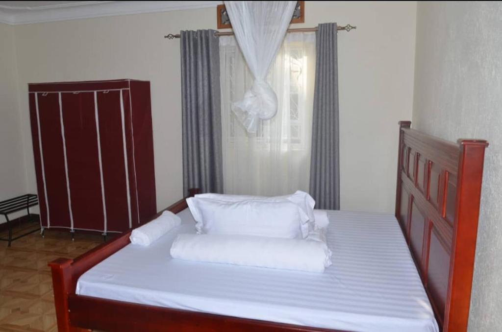 Una cama con sábanas blancas y almohadas en un dormitorio en Migingo Suites, en Entebbe