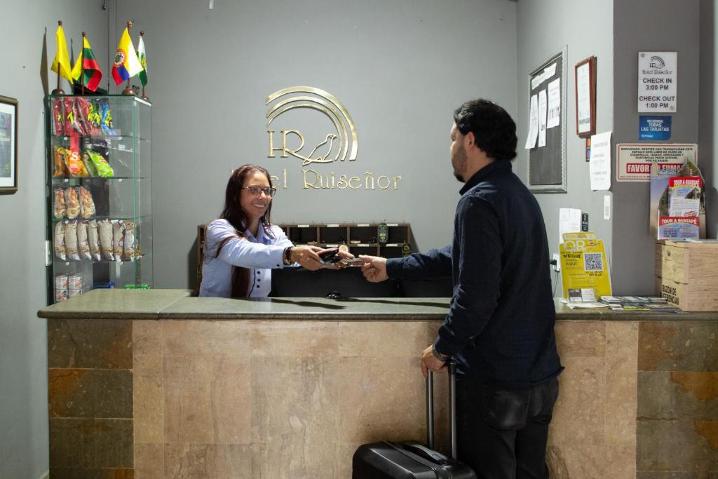 a man and a woman shaking hands at a counter at Hotel Ruiseñor Itagui in Itagüí