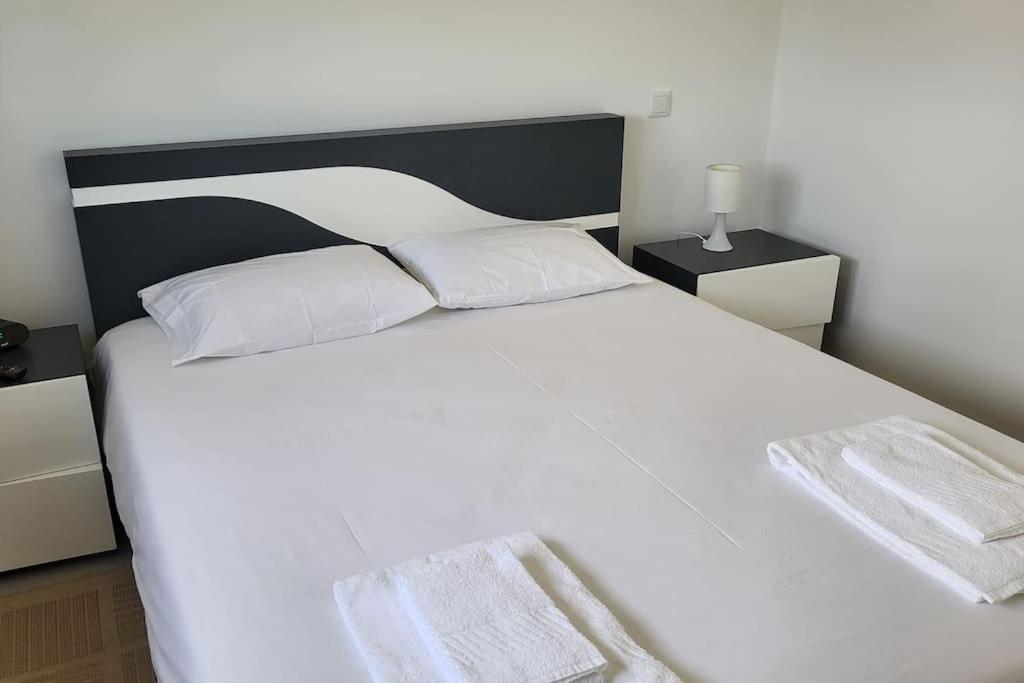 a white bed with white pillows and a black headboard at Jackie Apartment in Nazaré