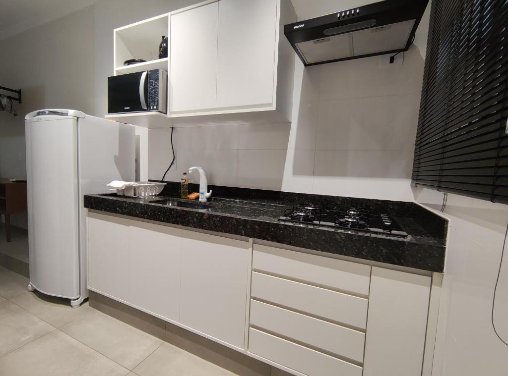 une cuisine avec des placards blancs et un comptoir noir dans l'établissement Apto Mobiliado Ar Cond Residencial Rios, à Barretos