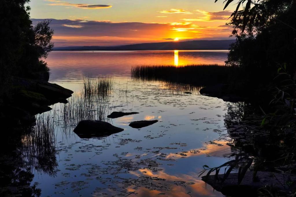 a sunset over a lake with rocks in the water at Shannonside - Stylish 5 Bed Marina home & 40ft mooring in Termonbarry