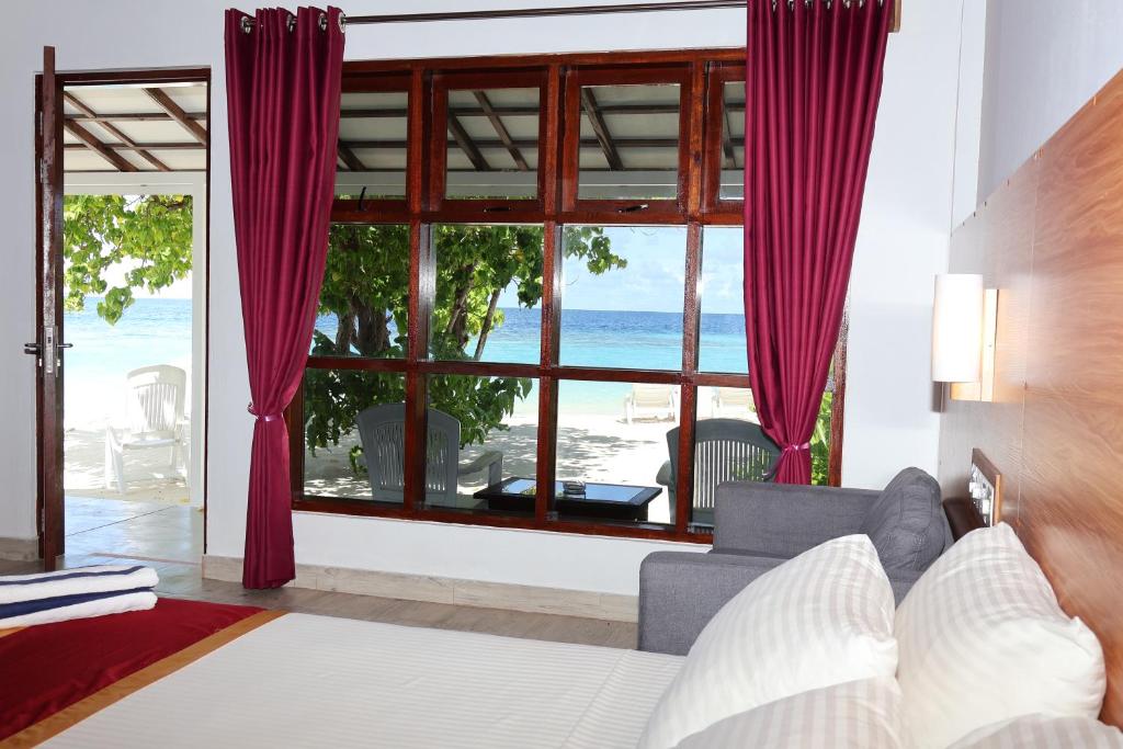 a bedroom with a view of the beach through a window at Lagoon View Maldives in Bodufolhudhoo