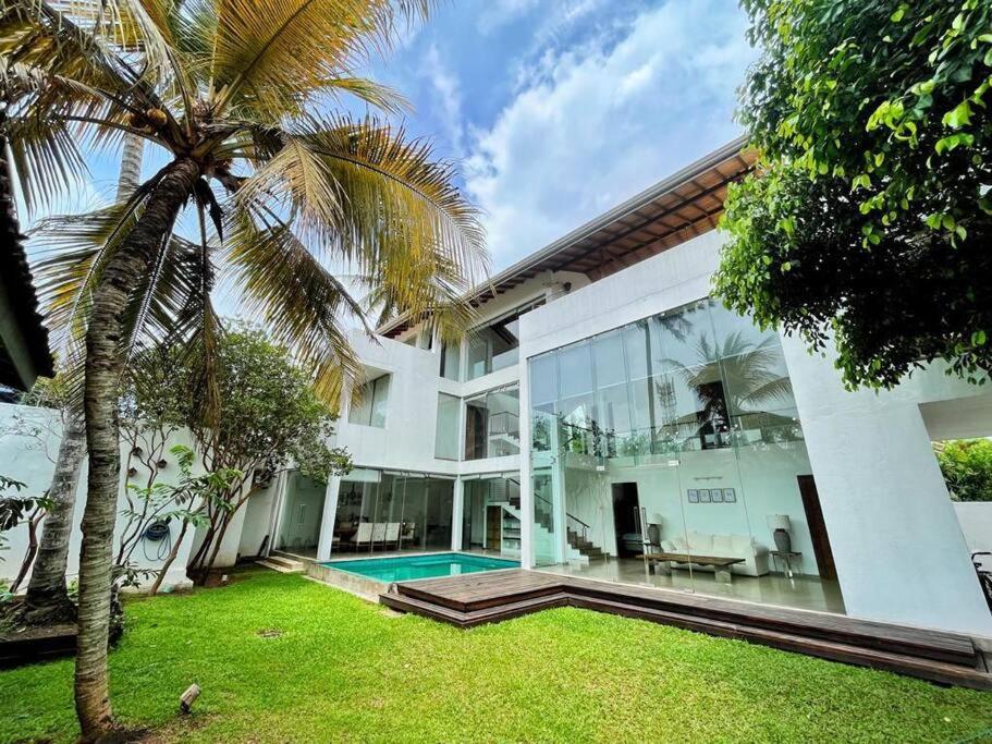 a white house with a palm tree and a swimming pool at Sanctuary Ceylon by Ceylon Spaces in Ratmalana South