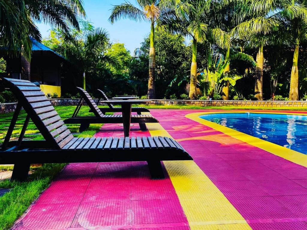 a pool with a bench and a table on a colorful rug at Raghuraj Enclave (AAI Farmhouse) in Alibag