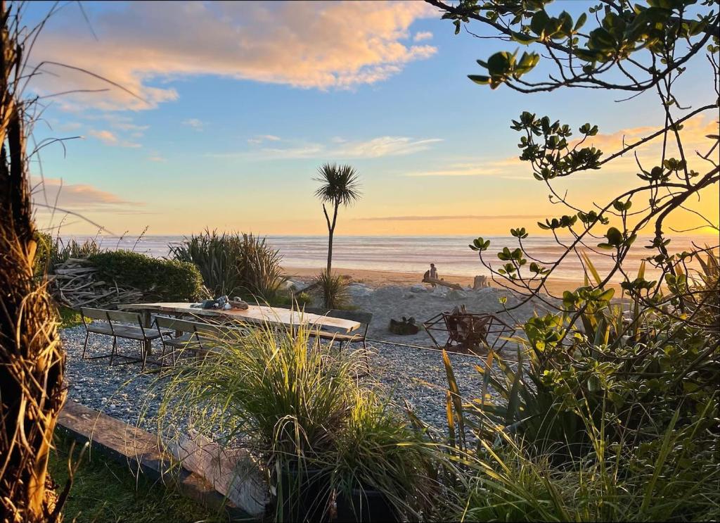 a beach with a picnic table and a palm tree at Drifting Sands Beachfront Retreat in Hokitika