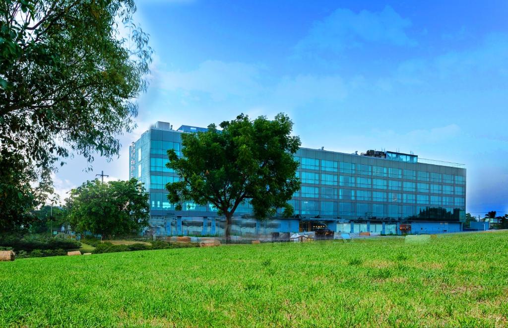 a building with a tree in front of a field at Svenska Design Hotel Kakinada in Kākināda