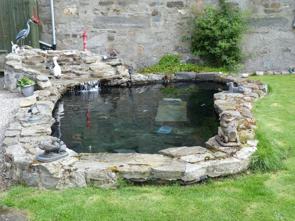 a pond in a yard with a stone wall at Waverley Villa in Grantown on Spey