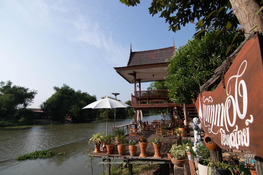 a building with plants and an umbrella next to a river at ทับทิมทอง โฮมสเตย์ in Ban Khlong Khut