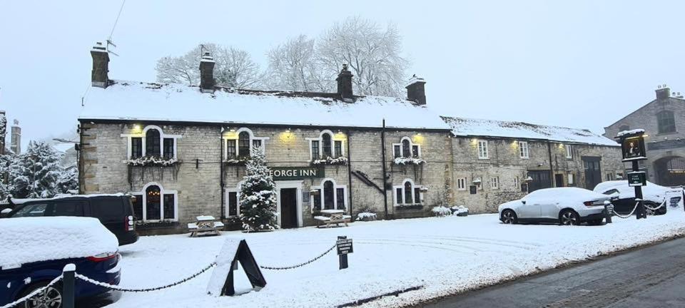 a building in the snow with cars parked in front at The George Inn at Tideswell in Tideswell