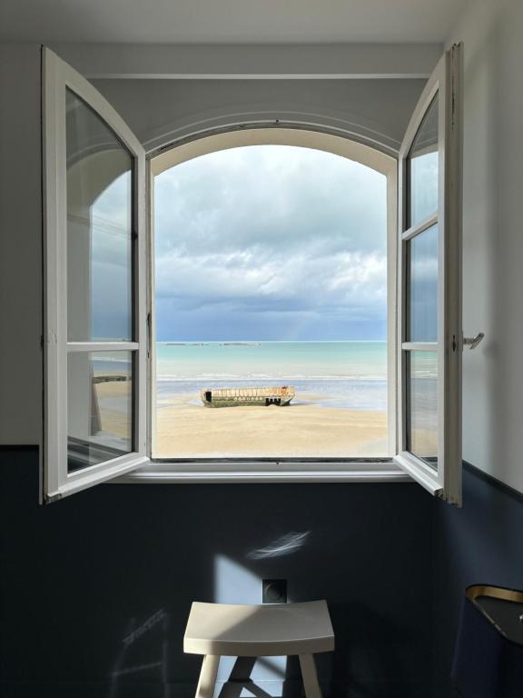 an open window with a view of the beach at Hôtel De La Marine in Arromanches-les-Bains