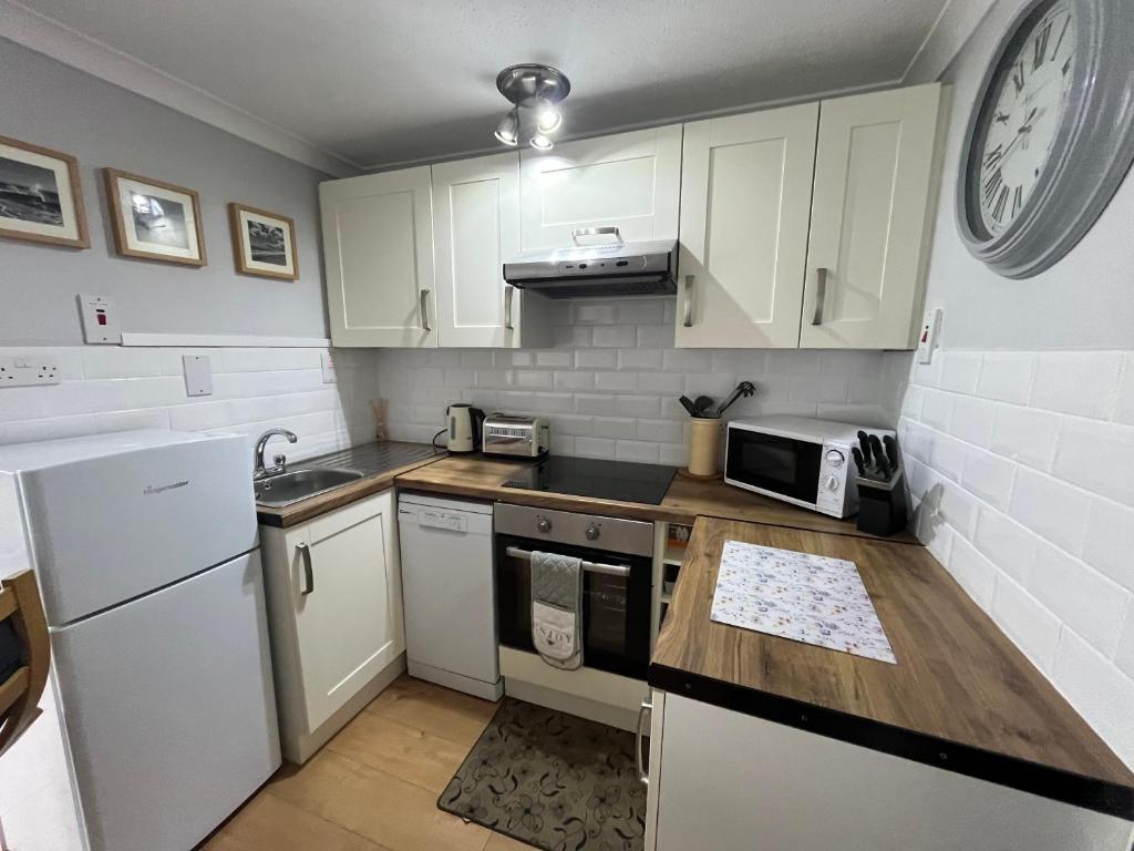a kitchen with white cabinets and a clock on the wall at 194, Belle Aire, Hemsby - Two bed recently renovated chalet, sleeps 4, pet friendly, free Wi-Fi and bed linen and towels included in Hemsby