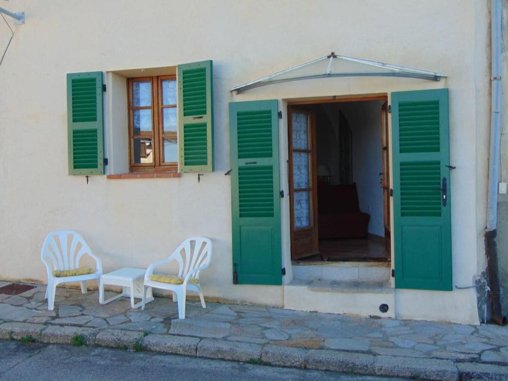 dwa krzesła siedzące przed budynkiem z zielonymi okiennicami w obiekcie Maison d'une chambre avec wifi a Belgodere w mieście Belgodère