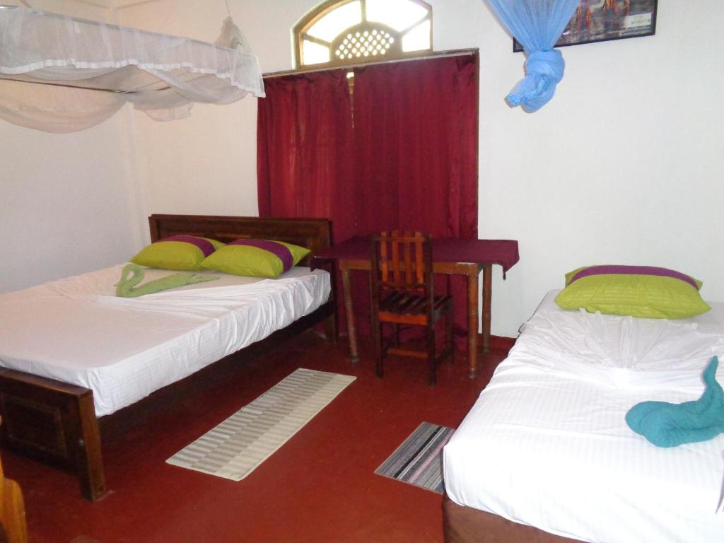 a room with two beds and a table and a chair at Wellawaya Rest House in Wellawaya