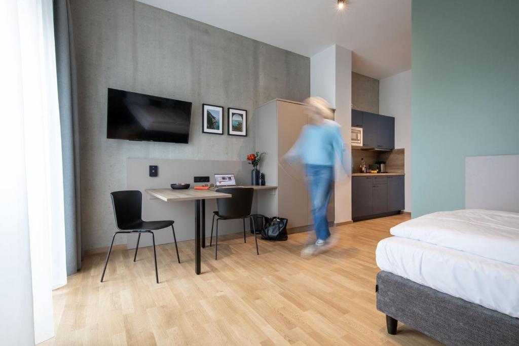 kobieta przechodząca przez pokój z łóżkiem i kuchnią w obiekcie Brera Serviced Apartments Singen w mieście Singen