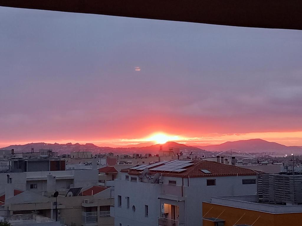 un coucher de soleil sur une ville avec des bâtiments et des montagnes dans l'établissement Maria house, à Athènes