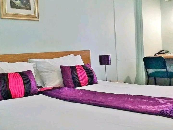 a white bed with pink and purple pillows on it at Brackendene Lodge in Gaborone