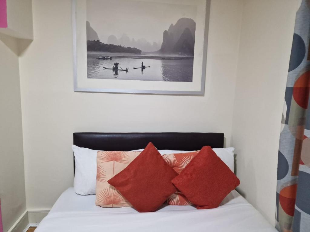 ein Bett mit roten Kissen und einem Bild an der Wand in der Unterkunft Deluxe 1-Bed Apartment in Greenford in Greenford