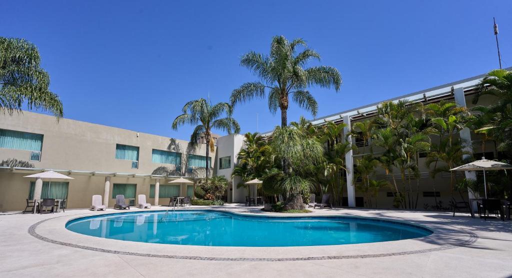 a swimming pool in front of a building with palm trees at Hotel Estancia Business Class in Guadalajara