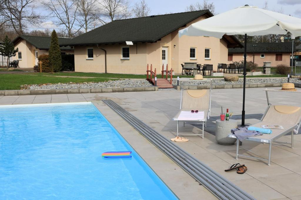a swimming pool with two chairs and an umbrella at Natur- und Aktivresort Senftenberg in Schipkau