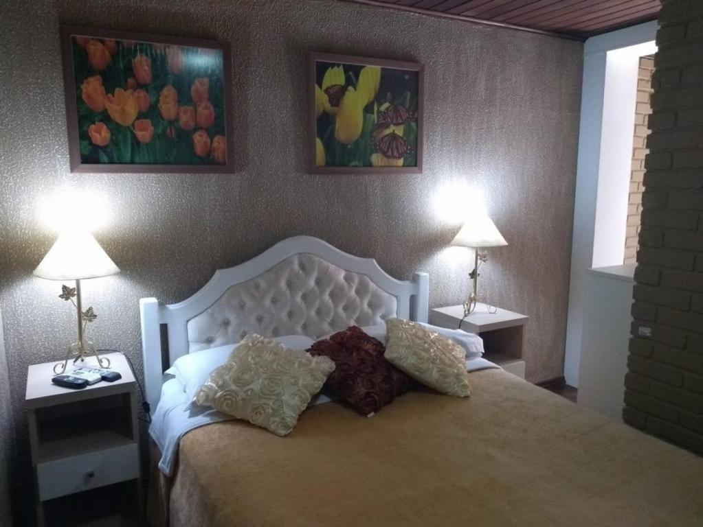 a bedroom with a bed with two lamps and paintings at Hospedagem Vida e Natureza in Gramado