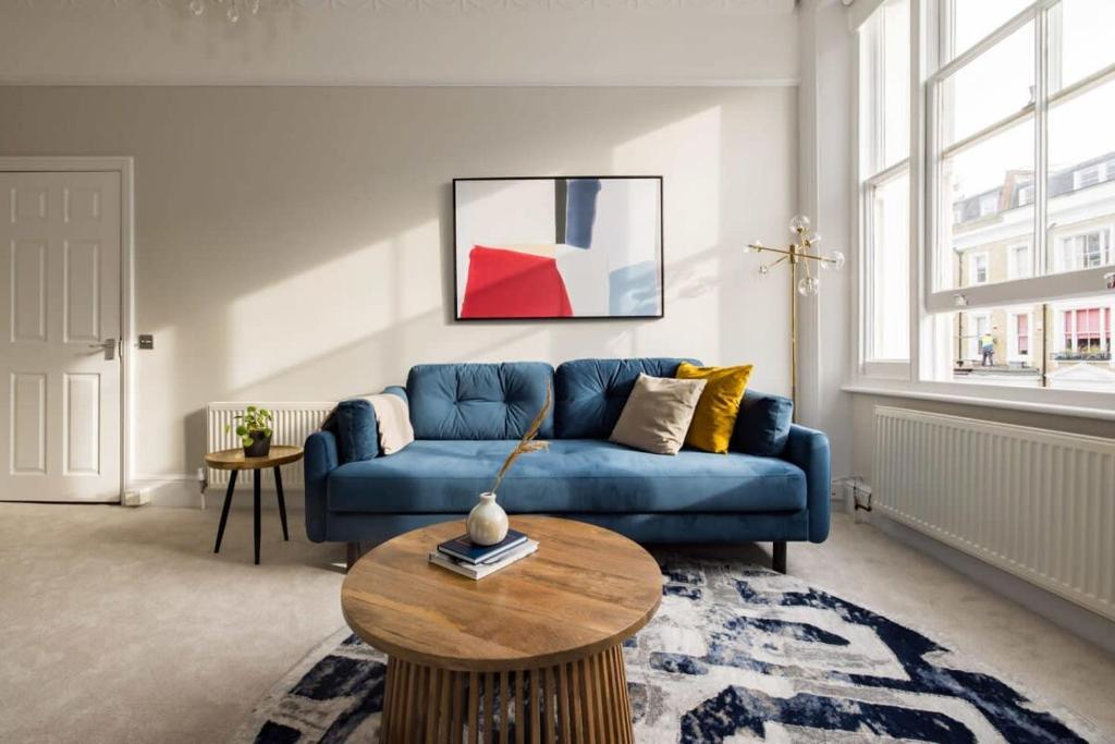 a living room with a blue couch and a table at Chic & Sunlit Earls Court Flat in London