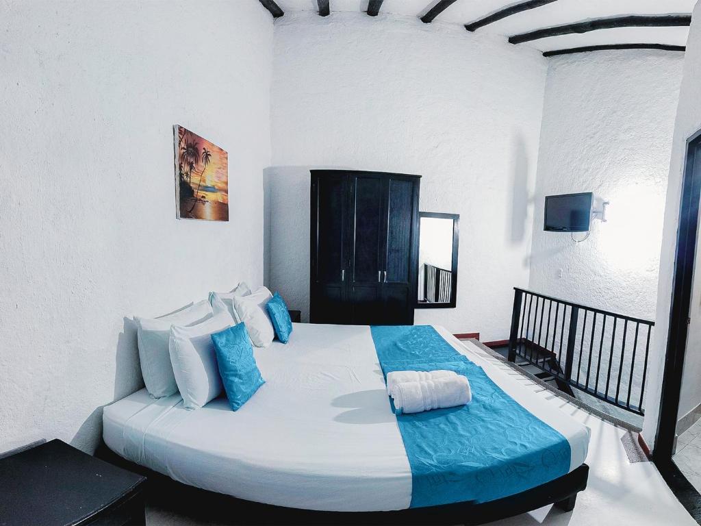 a white bedroom with a large bed with blue pillows at Hotel Sansiraka in Santa Marta