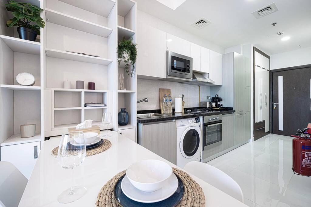a white kitchen with a table and white appliances at Dubai Sleek & Cozy Space in Dubai