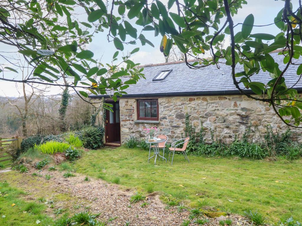 a stone cottage with a table and chairs in the yard at Little Tregarrick in Helston