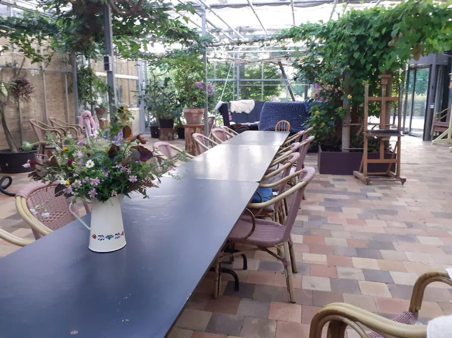 una mesa larga en un invernadero con un jarrón de flores en De Vlinderhof en Harskamp