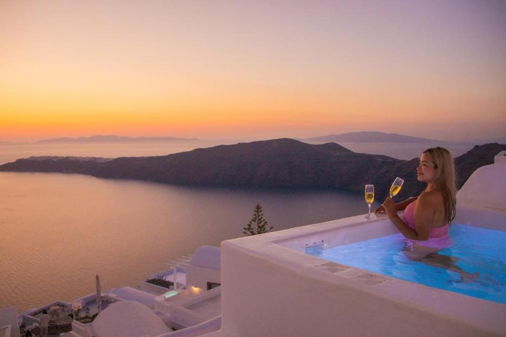 una mujer sentada en el borde de una piscina con una copa de vino en Esmi Suites Santorini en Imerovigli