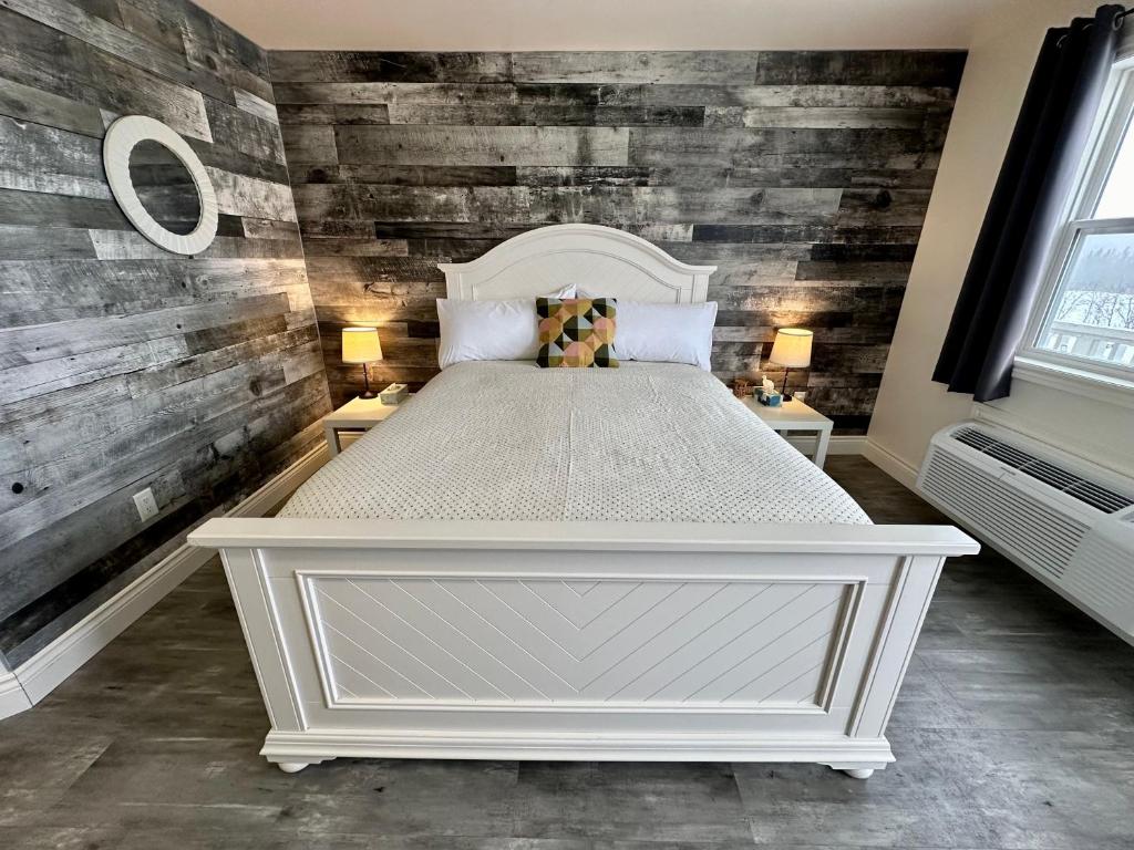 a bedroom with a white bed and wooden walls at Cheticamp Outback Inn in Chéticamp