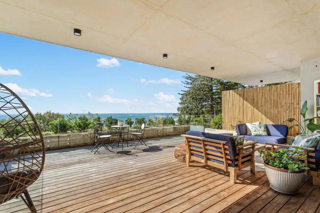a wooden deck with a couch and chairs on it at Ocean Views, Deck and Parking at Beach Apartment in Collaroy