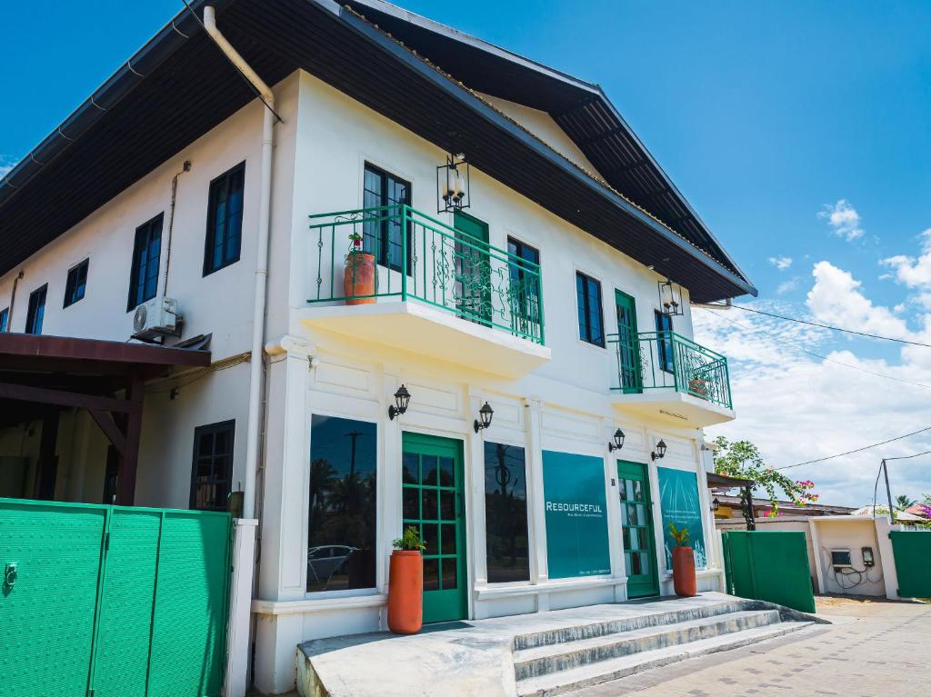 a white building with green windows and a balcony at Cozy and quirky Wolf Apartment in Paramaribo