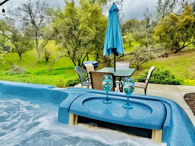 a table with glasses and an umbrella next to a swimming pool at Lighthouse Suite Pet Friendly Hot Tub Sleeps 4 in Coarsegold