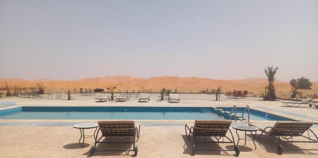 uma piscina com cadeiras e mesas no deserto em SANDSTAR PALACE em Merzouga