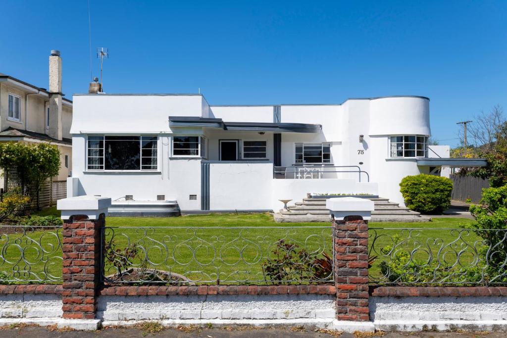 a white house with a brick fence at Art Deco Charm - Amazing River Views Inner City in Gisborne
