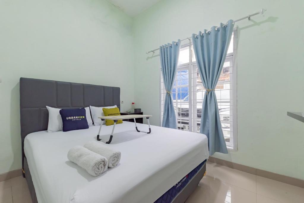 a bedroom with a large bed with blue curtains and a window at Urbanview Hotel Nakasya Burangrang in Bandung