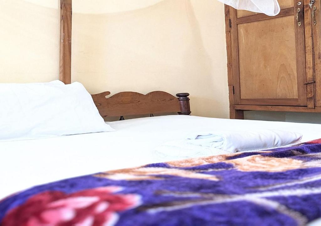 Una cama con sábanas blancas y una manta colorida. en Sea Hotel, en Pangani
