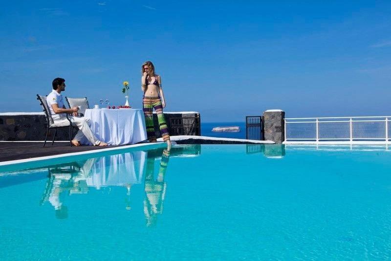 Ein Mann und eine Frau sitzen an einem Tisch neben einem Pool in der Unterkunft Beautiful Santorini Villa - 2 Bedroom Villa - Panoramic Caldera Sea Views and Private Plunge Pool - Megalochori in Megalochori