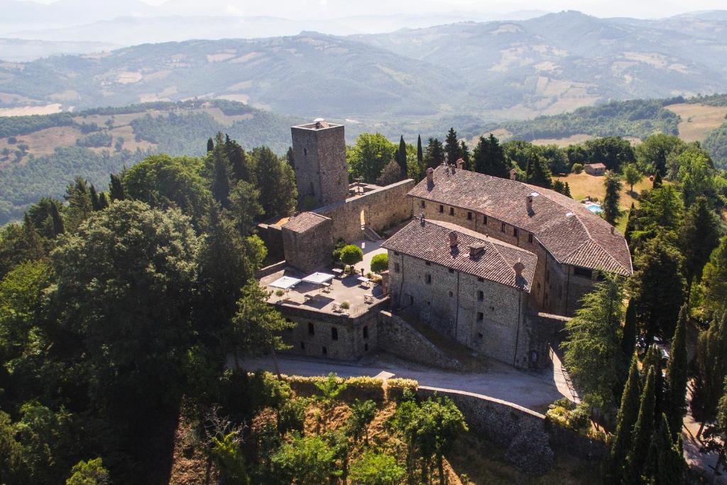 un antiguo edificio en una colina con montañas en el fondo en Castello Di Petroia Dimora d'Epoca, en Gubbio