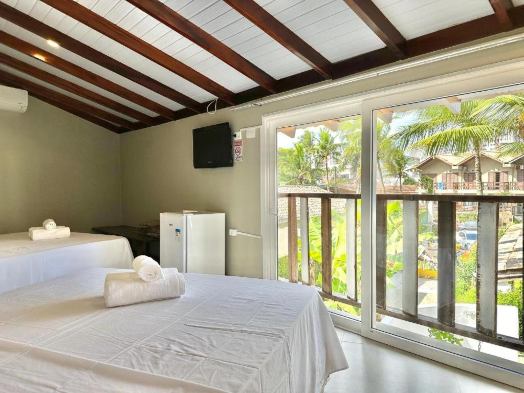 ein Schlafzimmer mit einem weißen Bett und einem großen Fenster in der Unterkunft Casa Canoa Hotel Boutique à Beira-mar com Piscina e Café da manhã in Guarujá