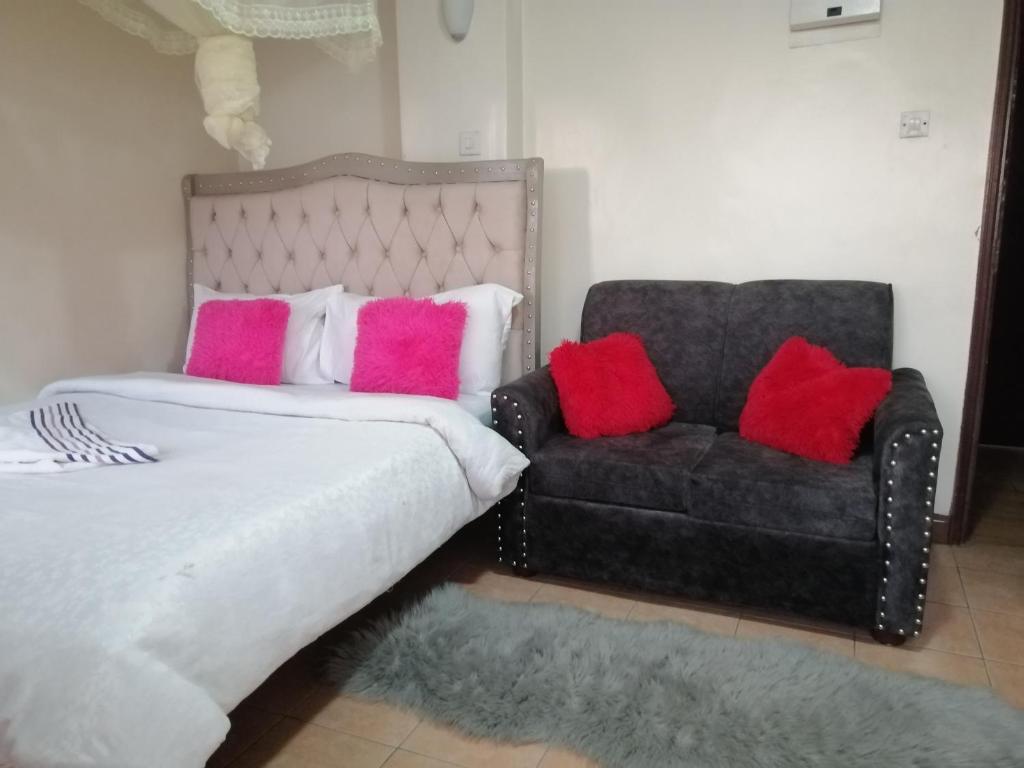a bed with pink and red pillows next to a couch at Joy suites emeli in Nairobi
