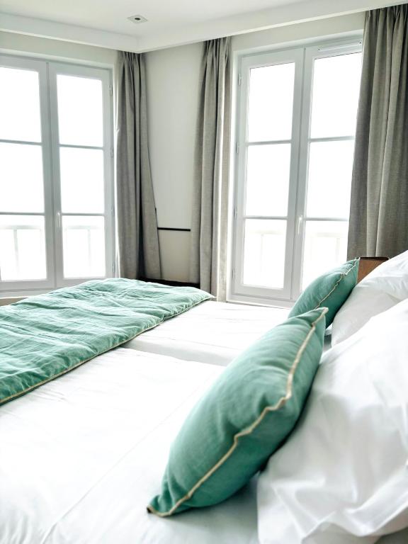 a bed with green pillows on it in a room with windows at Hôtel De La Marine in Arromanches-les-Bains