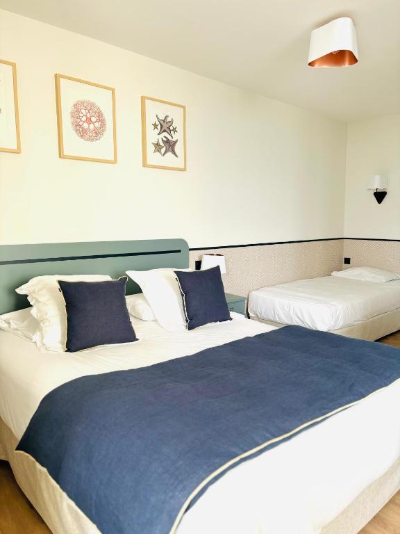 a bedroom with two beds with blue and white pillows at Hôtel De La Marine in Arromanches-les-Bains