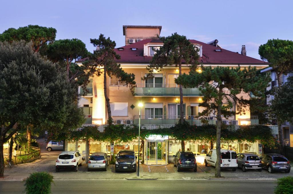 un grande edificio con auto parcheggiate in un parcheggio di Hotel Mimosa a Lignano Sabbiadoro