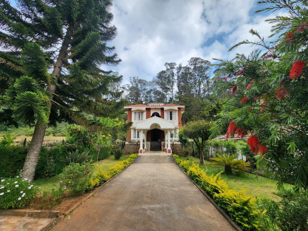 una entrada que conduce a una casa blanca con árboles en Narmada Holiday Home, en Ooty
