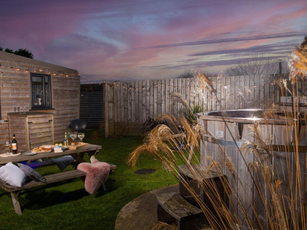 een achtertuin met een tafel, een grill en een hek bij Chalet Wheal Jewel Hot Tub Lodge by Interhome in Helston